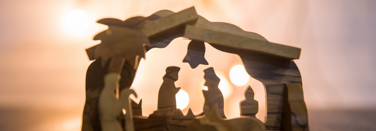 Wooden nativity scene glowing against warm Christmas lights