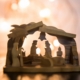 Wooden nativity scene glowing against warm Christmas lights