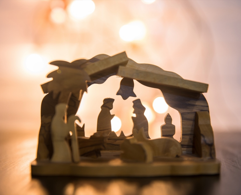 Wooden nativity scene glowing against warm Christmas lights